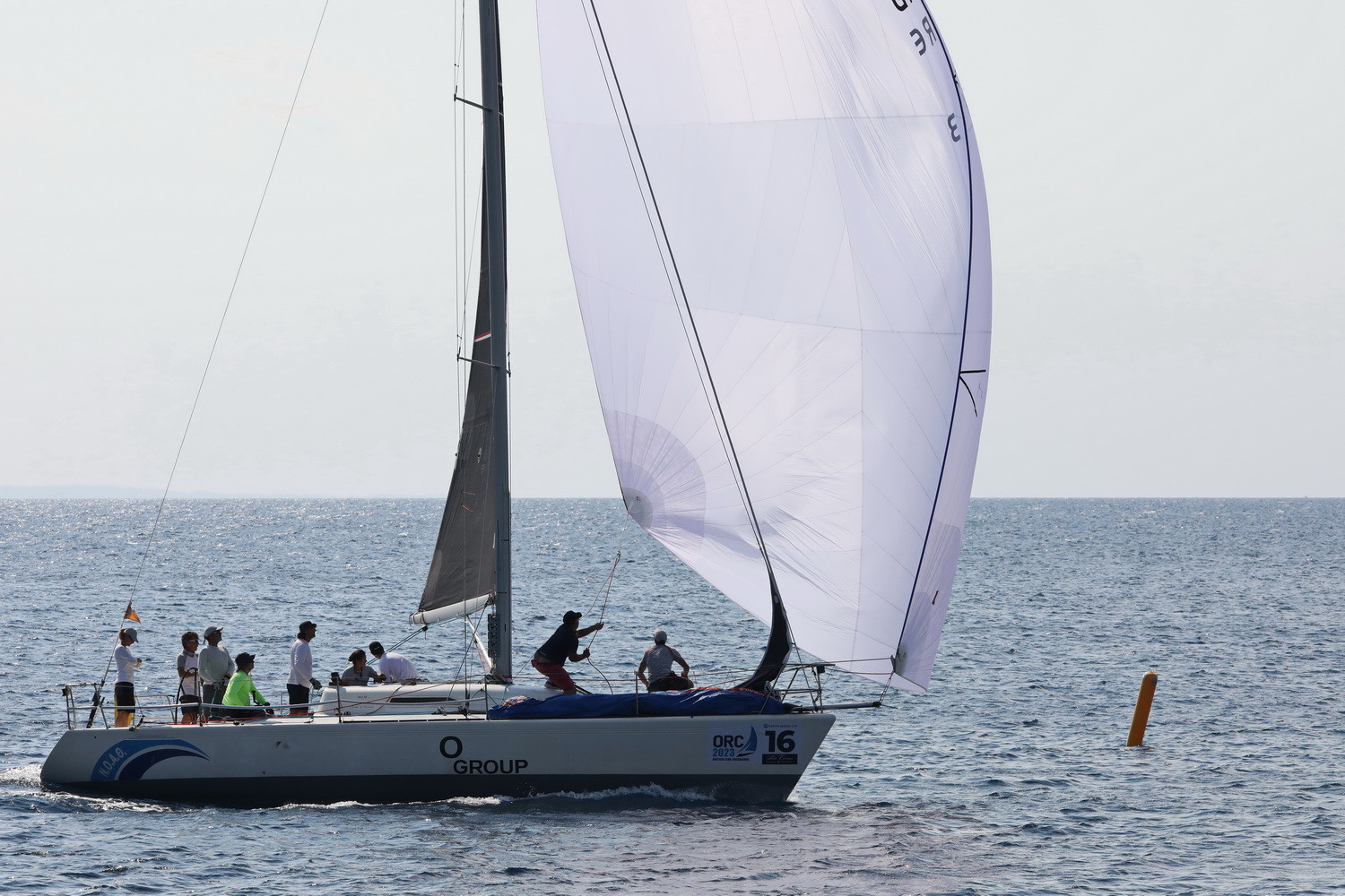 Sailing boat, white spinnaker sail wit a few people on board.